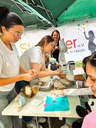 Kinder üben beim Sommerfest in der Teddy-Klinik, Stofftiere zu verbinden.
